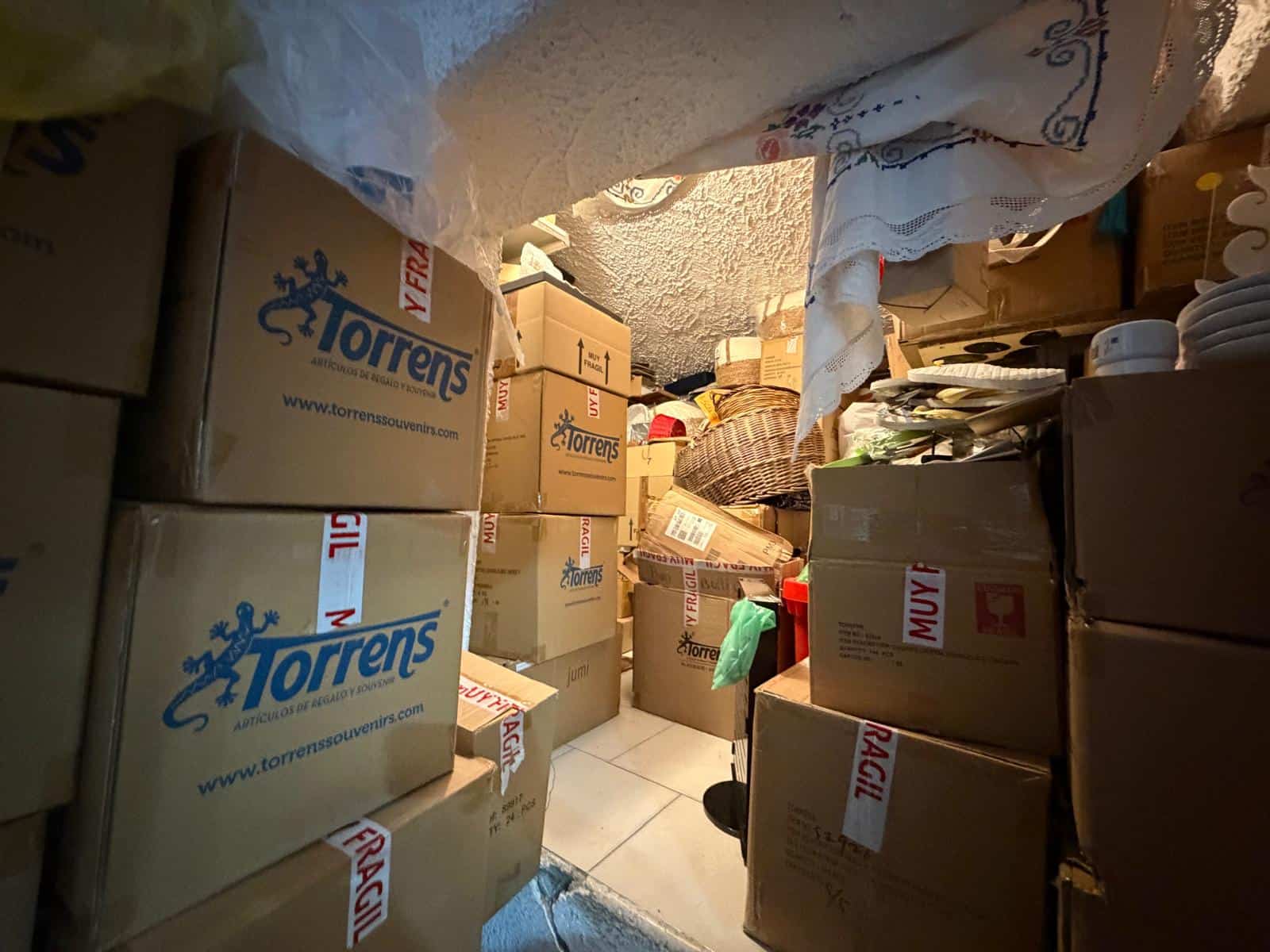 Scatola di cartone piena di oggetti e scatoloni in un magazzino o deposito, con etichette e imballaggi vari.