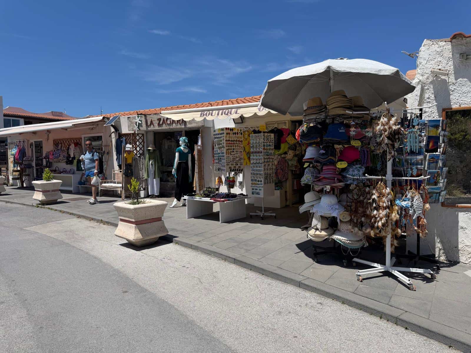 Passeggiata in un mercato all'aperto con bancarelle di souvenir e accessori, sotto un cielo azzurro e soleggiato, con negozi tradizionali e turisti che esplorano le offerte locali.