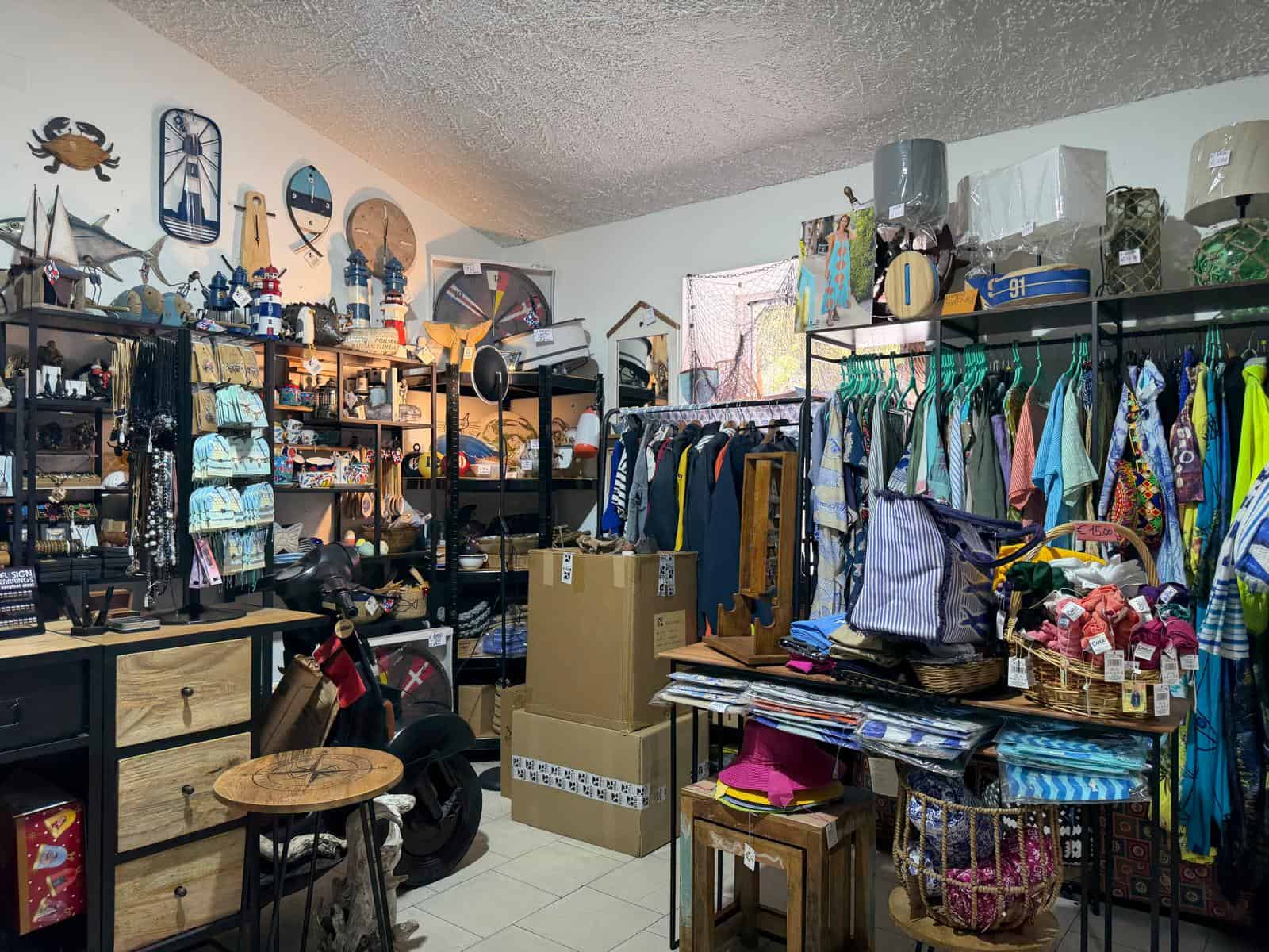 Vestiti e accessori in vendita in un negozio di seconda mano, con scaffali pieni di abbigliamento, borse e decorazioni vintage, creando un ambiente accogliente e ben organizzato.