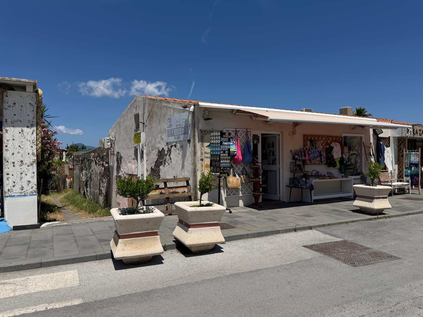 Vicolo con negozio di artigianato locale e panchine in cemento, facciata di un edificio storico con pareti in pietra e decorazioni colorate, sotto un cielo azzurro con poche nuvole.
