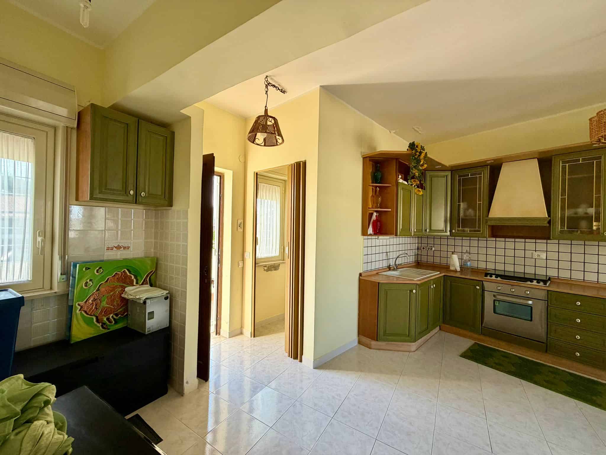 Cucina abitabile con mobili verdi, forno e piano cottura, illuminata da luce naturale, in un appartamento luminoso e accogliente.