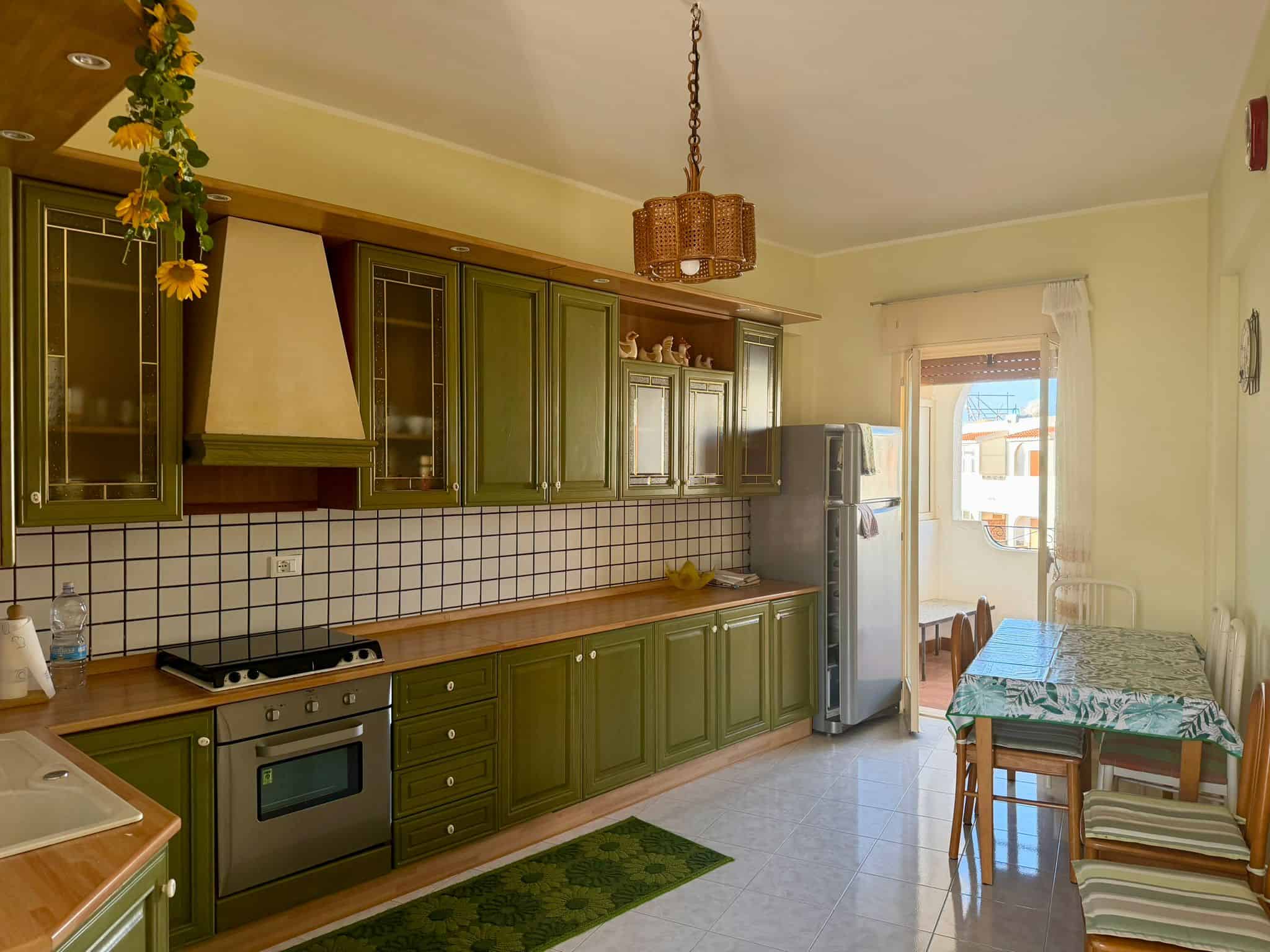 Cucina abitabile con mobili verdi, piano in legno, frigorifero e tavolo con sedie, ambiente luminoso e accogliente, ideale per cucinare e mangiare in famiglia.