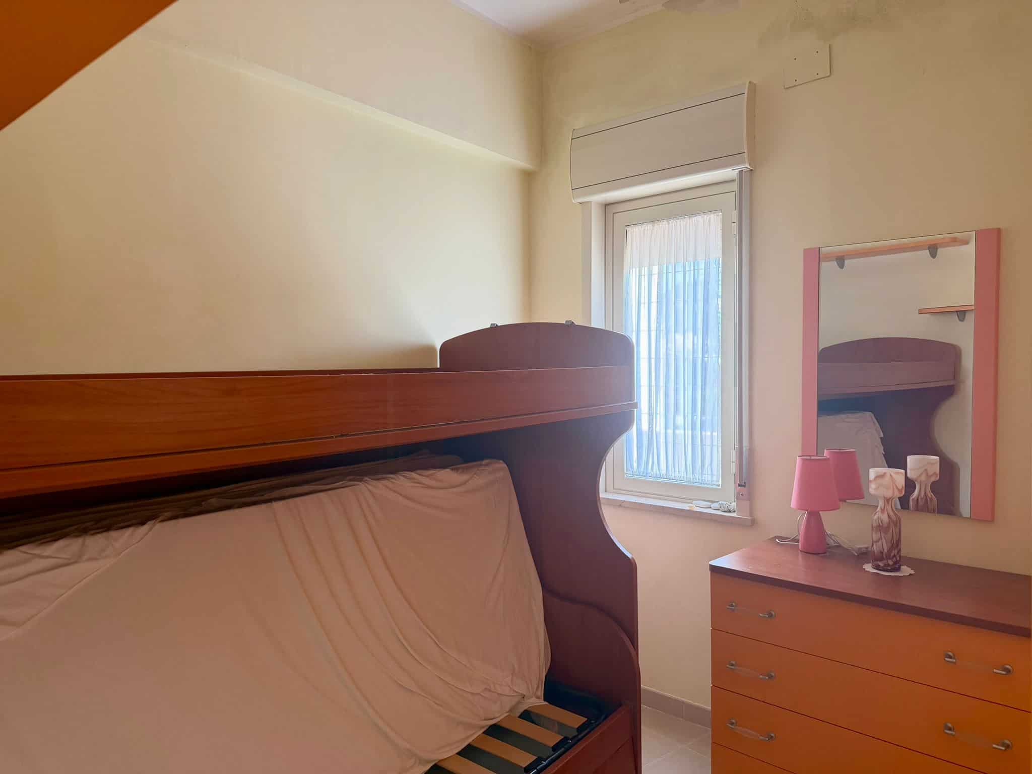 Letto a soppalco in una camera da letto con finestra e mobili in legno, ambiente luminoso e accogliente.