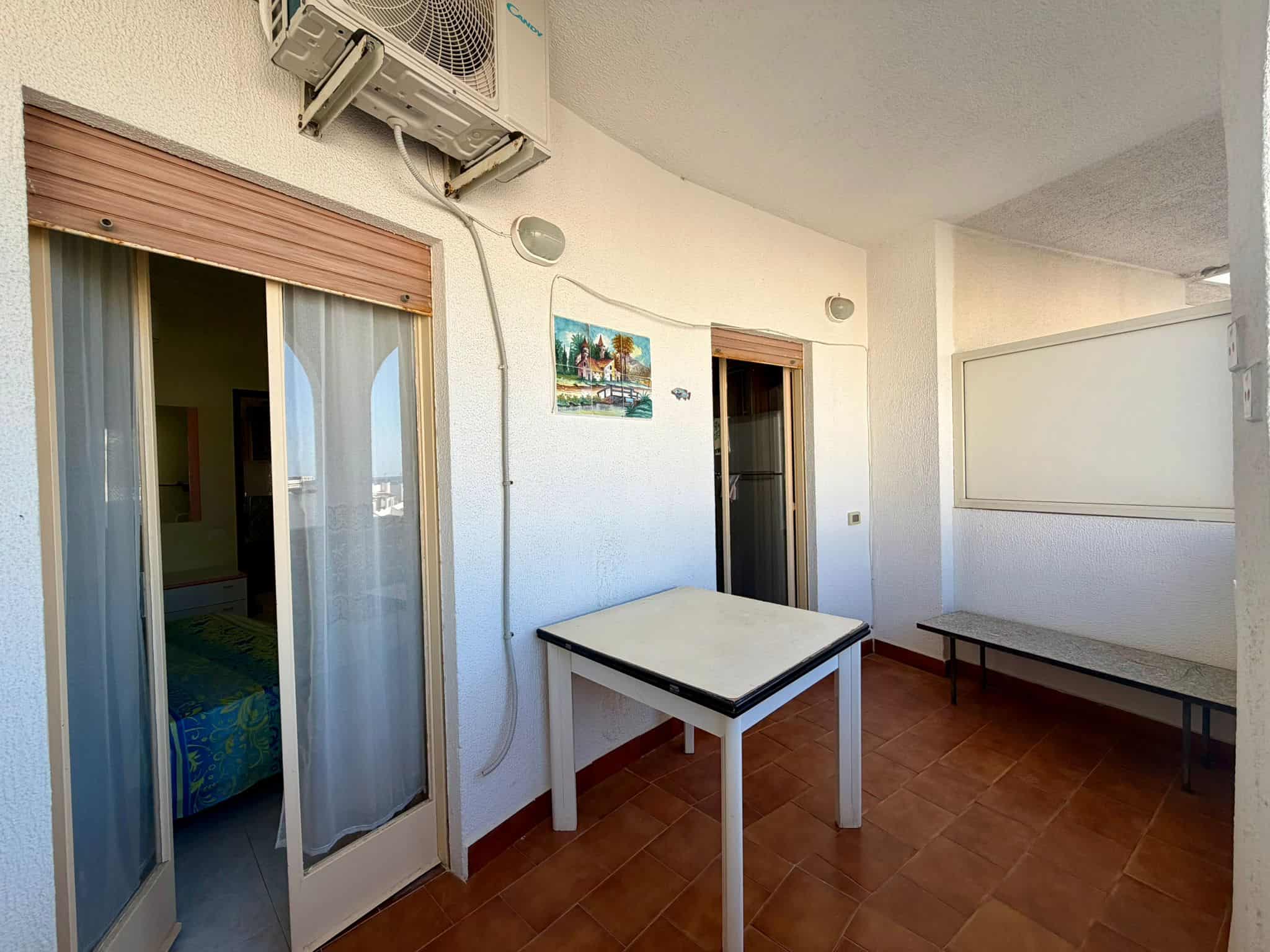 Balcone di un appartamento con vista sul mare, arredato con tavolo e panca, ideale per relax e convivialità, in zona residenziale vicino alla spiaggia, con aria condizionata e decorazioni colorate.