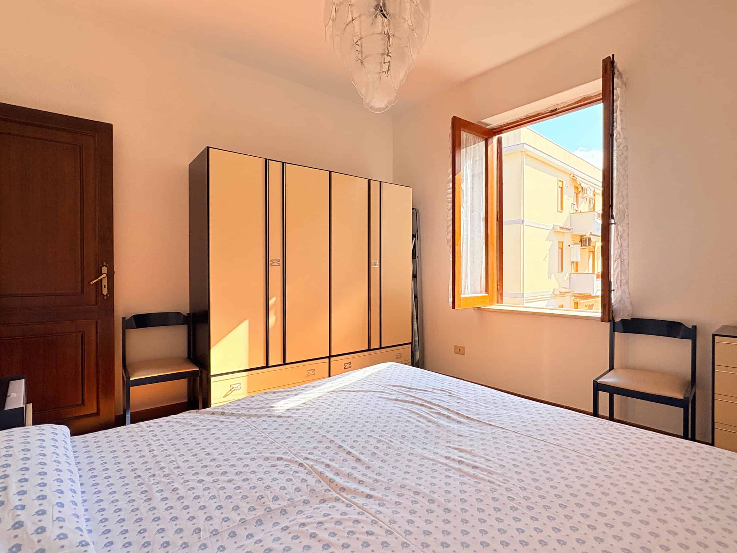 Ampia camera da letto luminosa con armadio a sei ante, finestra aperta che lascia entrare luce naturale, arredamento semplice e confortevole, ideale per soggiorni rilassanti.