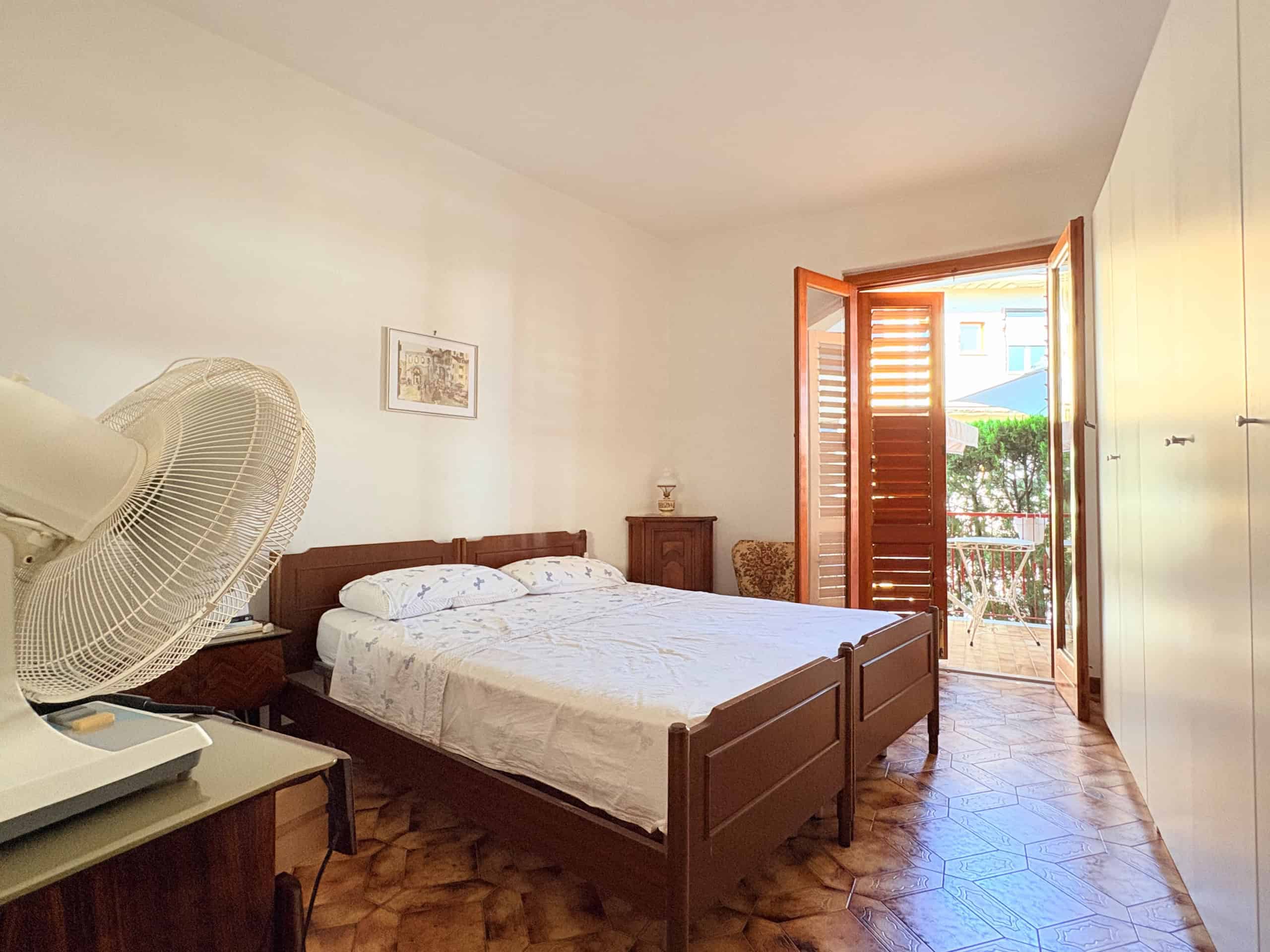 Ampia camera da letto con letto matrimoniale, armadio e balcone con vista su giardino, in stile semplice e luminoso, ideale per soggiorni rilassanti e confortevoli.