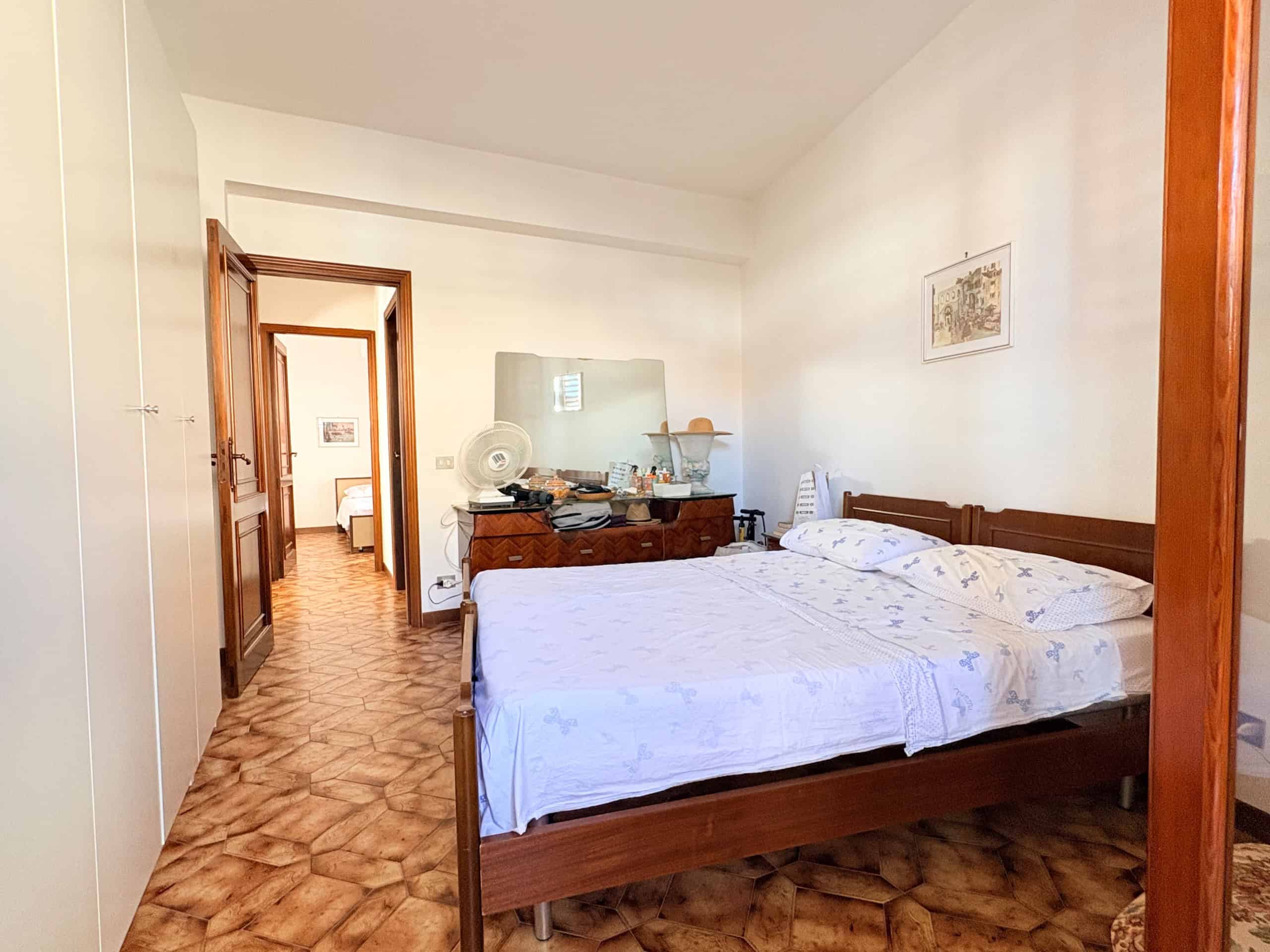 Letto matrimoniale in camera da letto con arredi classici, pareti bianche e pavimento in piastrelle di ceramica, ambiente luminoso e accogliente, ideale per soggiorni confortevoli.