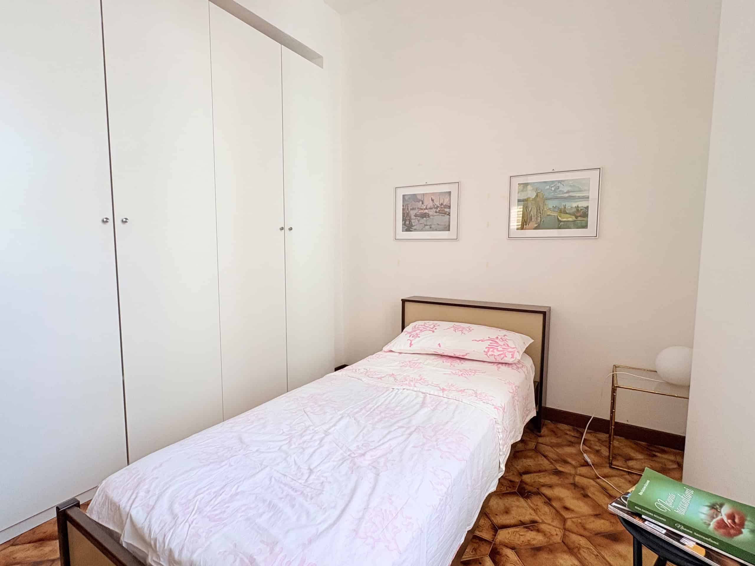 Una stanza da letto luminosa con letto singolo, armadio a muro bianco e decorazioni semplici, ideale per affitti a breve termine o residenze confortevoli.
