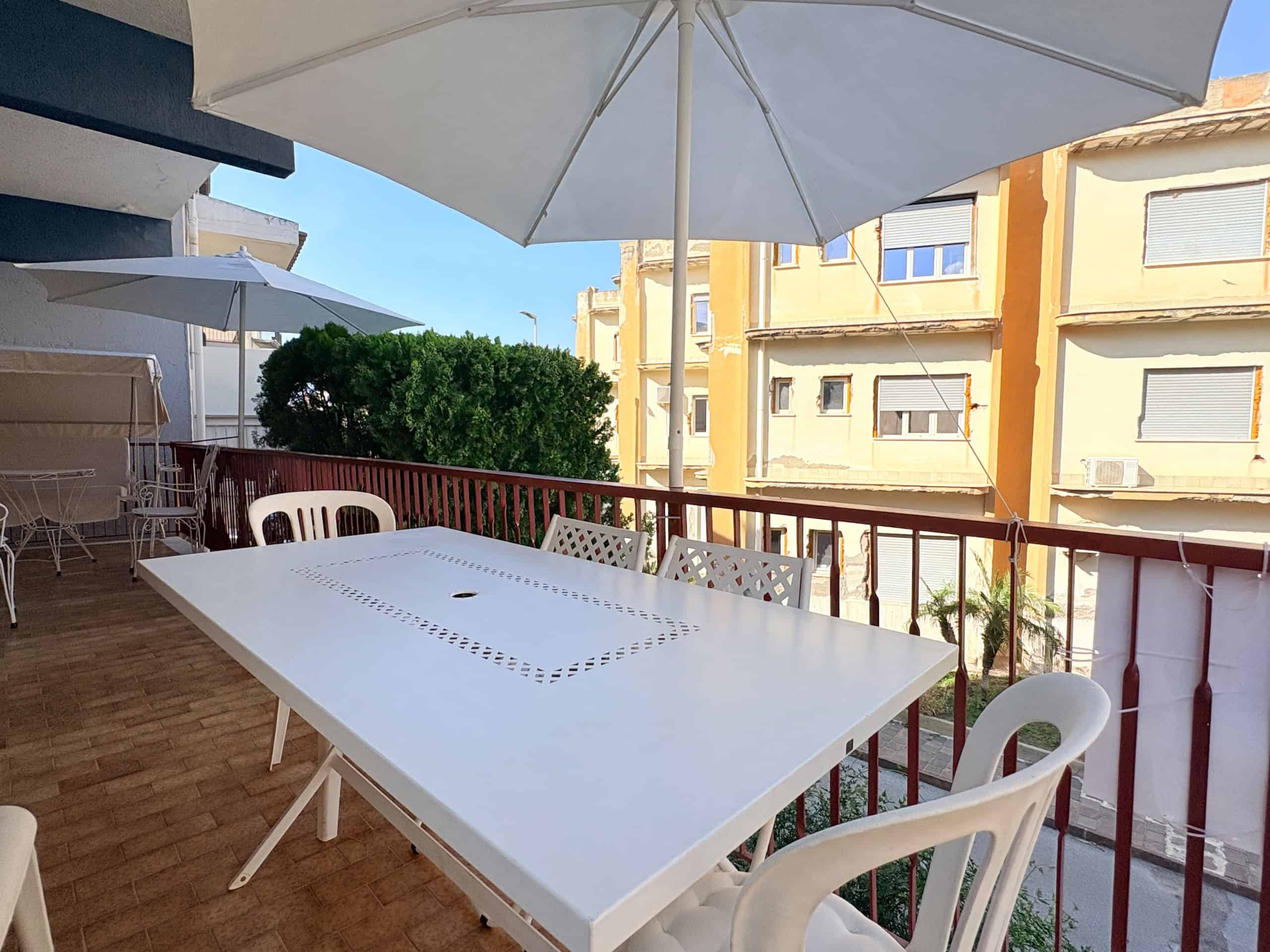 Terrazza con tavolo e sedie in plastica, ombrellone parasole, vista su edifici residenziali, ambiente esterno soleggiato, spazio relax all'aperto.