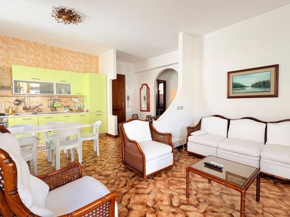 Una vista del soggiorno e cucina di un appartamento moderno con arredi eleganti, pareti bianche, pavimento in piastrelle marroni e mobili in stile classico, ideale per affitti turistici o residenziali.