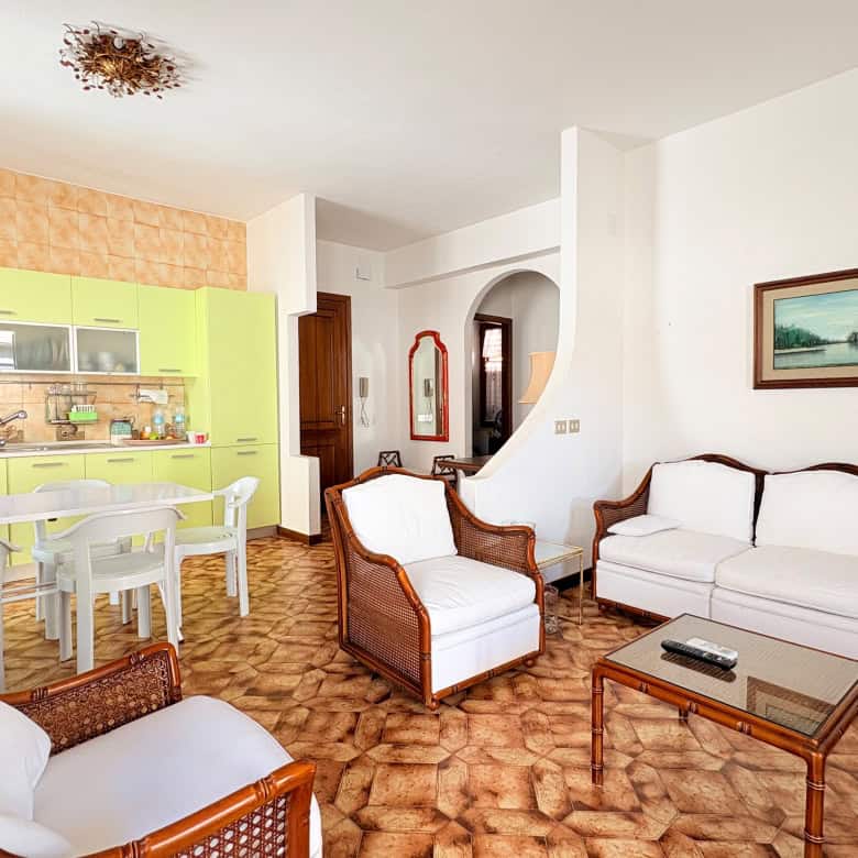 Una vista del soggiorno e cucina di un appartamento moderno con arredi eleganti, pareti bianche, pavimento in piastrelle marroni e mobili in stile classico, ideale per affitti turistici o residenziali.