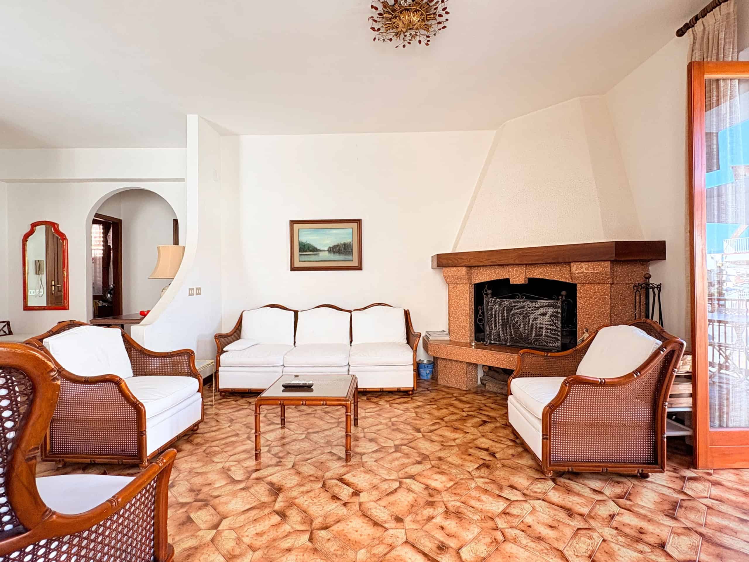 Elegante soggiorno con camino in pietra, divani in tessuto bianco e mobili in legno, ideale per relax e convivialità in una casa accogliente e ben arredata.