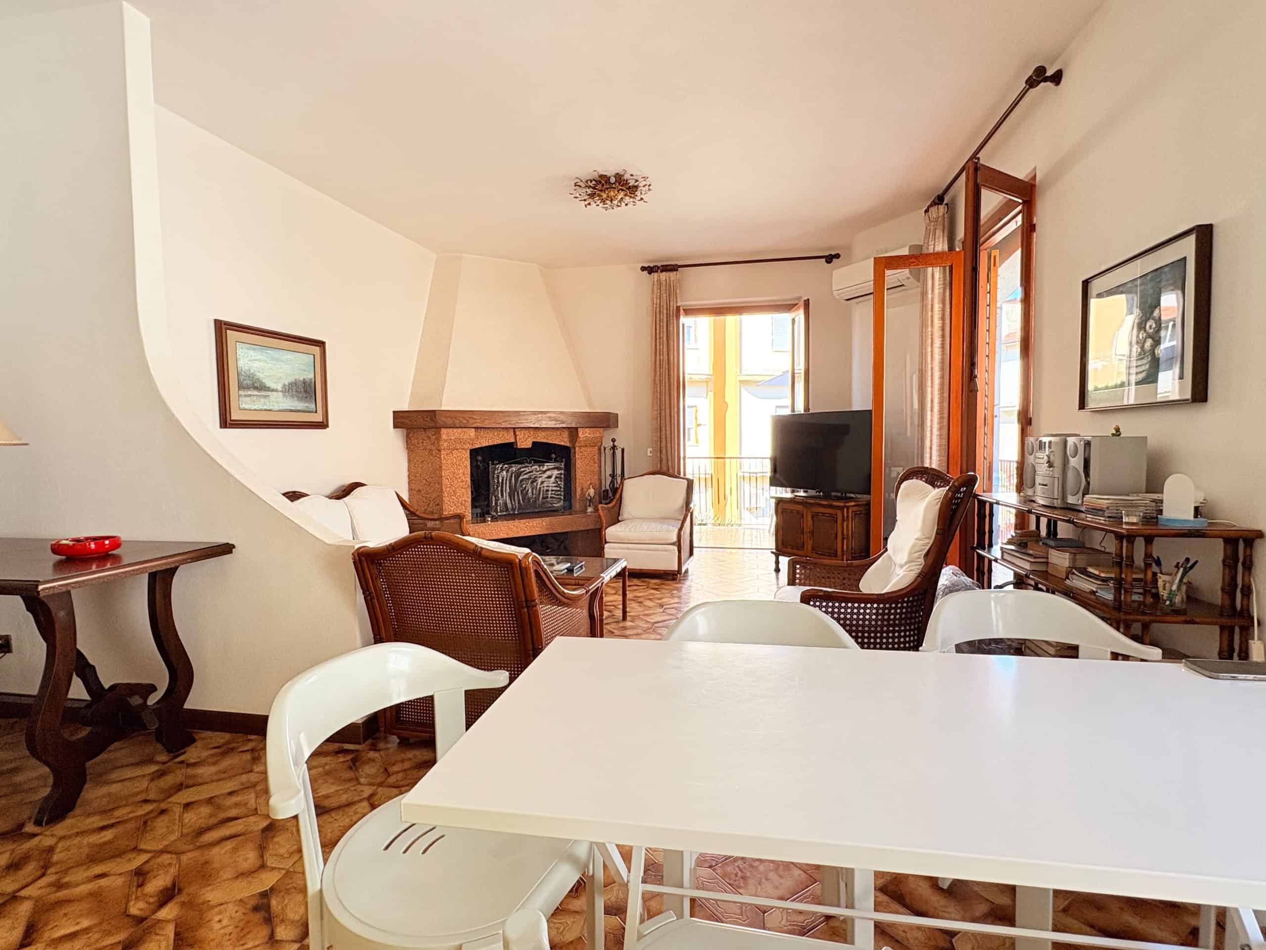 Spazioso soggiorno con camino, mobili eleganti e accesso a un balcone soleggiato, ideale per vivere momenti di relax e convivialità in un ambiente accogliente e ben arredato.