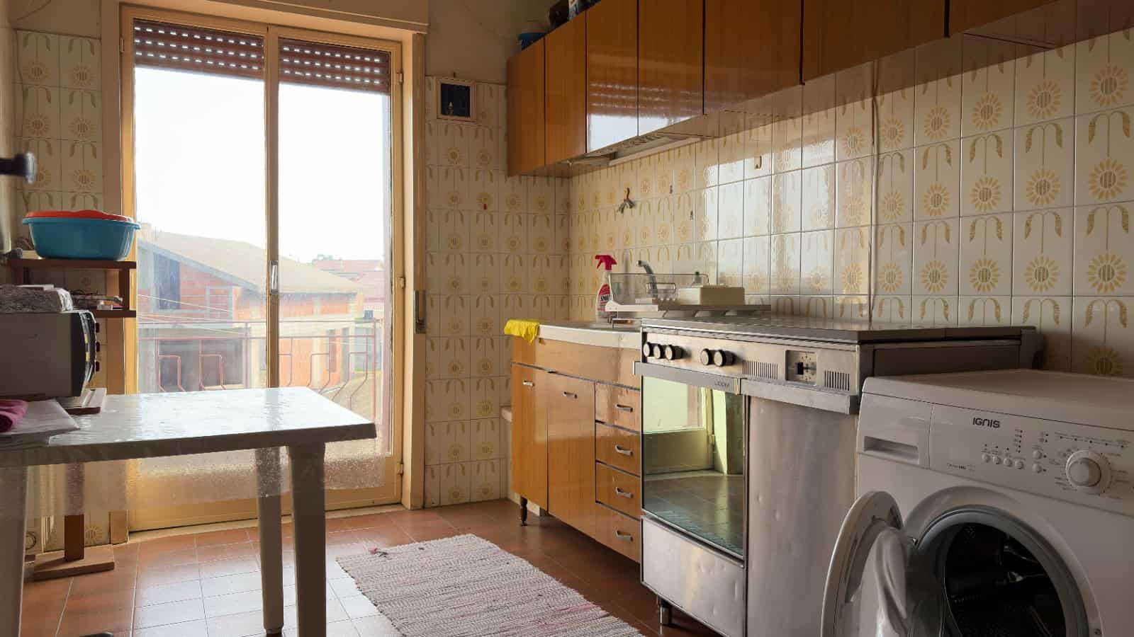 Pannello di cucina con elettrodomestici e accessori, vista sulla terrazza con edifici residenziali, ambiente domestico funzionale e ben illuminato, ideale per la vita quotidiana.