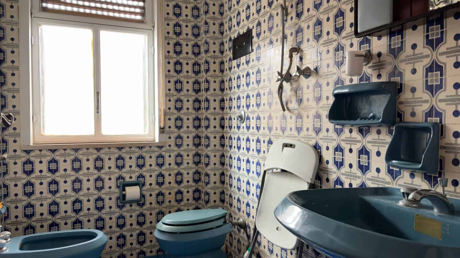 Lavabo e servizi igienici in stile vintage con piastrelle decorative blu e bianche, finestra naturale, ambiente pulito e ben illuminato, ideale per immagini di arredo bagno in vendita o affitto.