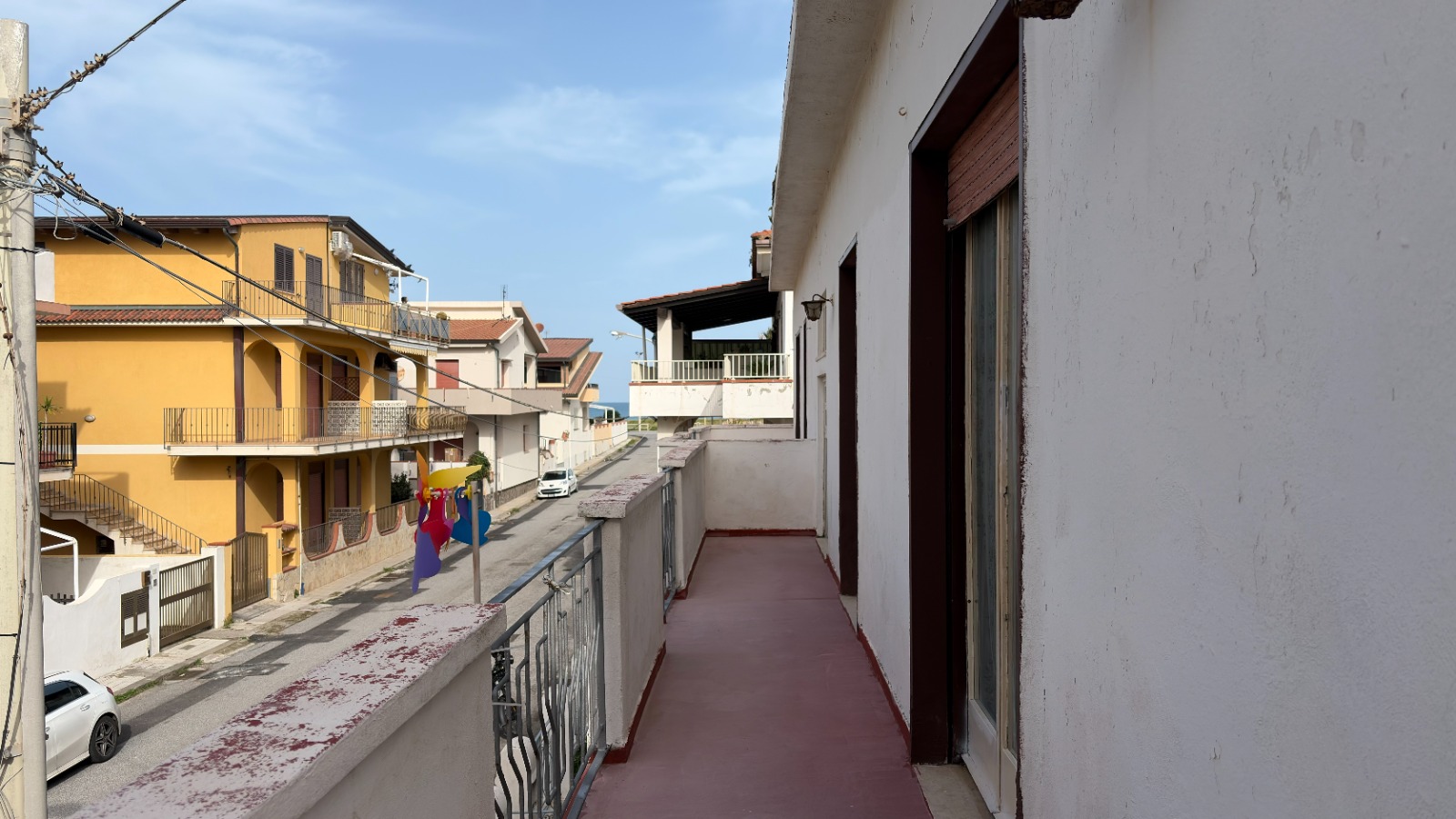 Balcone di un appartamento con vista su strada urbana, edifici residenziali colorati e cielo sereno, ideale per chi cerca immobili in vendita o affitto in zona urbana.