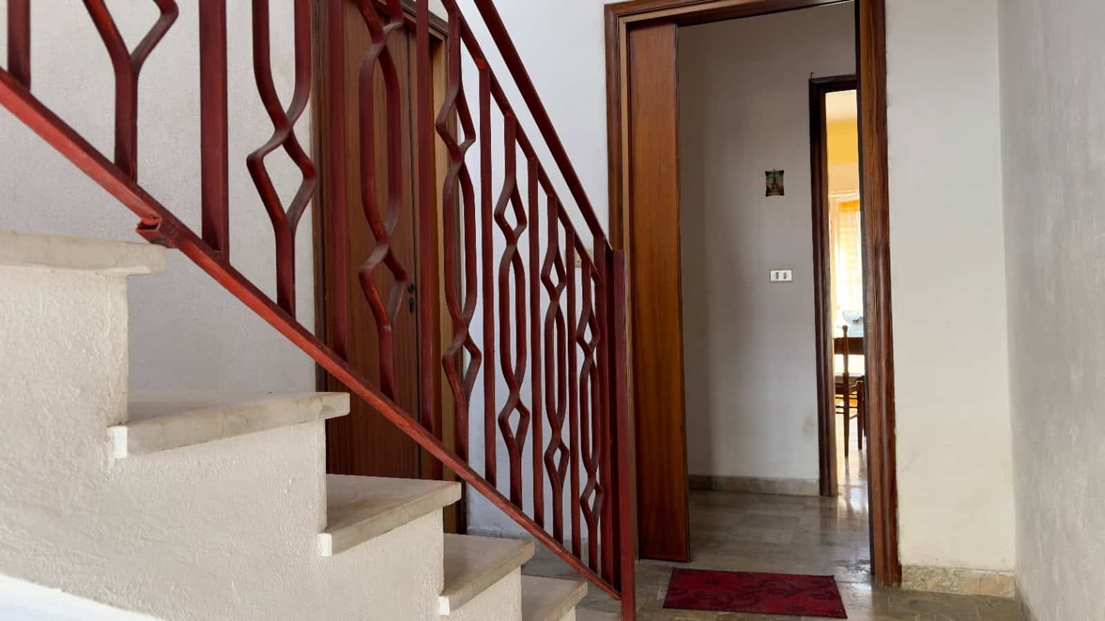 Scala interna con ringhiera in ferro battuto e pareti bianche, ingresso a un appartamento o casa.