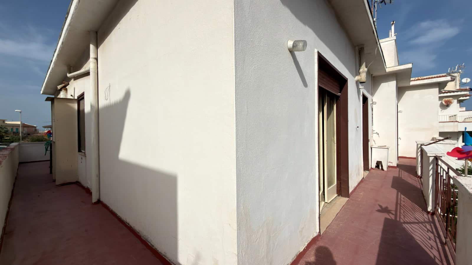 Balcone di un appartamento con vista sulla città, pavimentato in piastrelle rosse e pareti bianche, con accesso tramite porta finestra e ringhiera in metallo. Ideale per relax e momenti all'aperto.