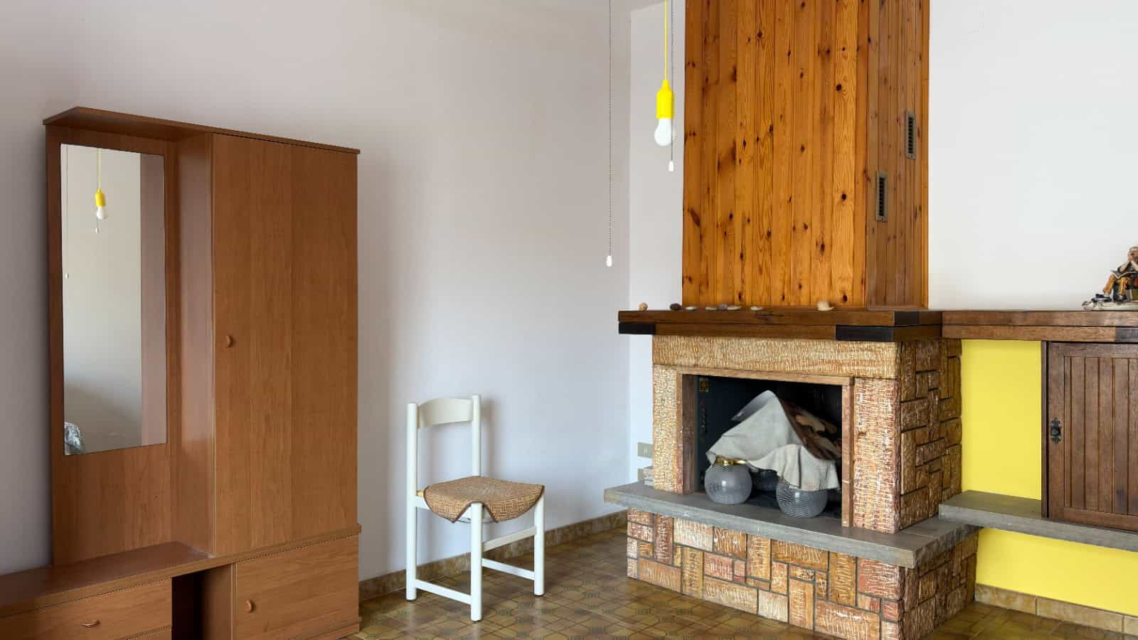 Interno di una casa con camino in mattoni e mobili in legno, ambiente accogliente e rustico.