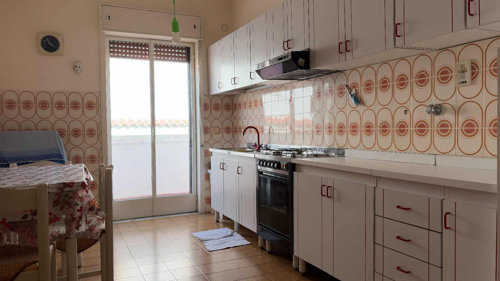 Cucina abitabile con mobili bianchi, piano cottura e accessori, in un ambiente luminoso e accogliente con pareti decorate in stile retrò.