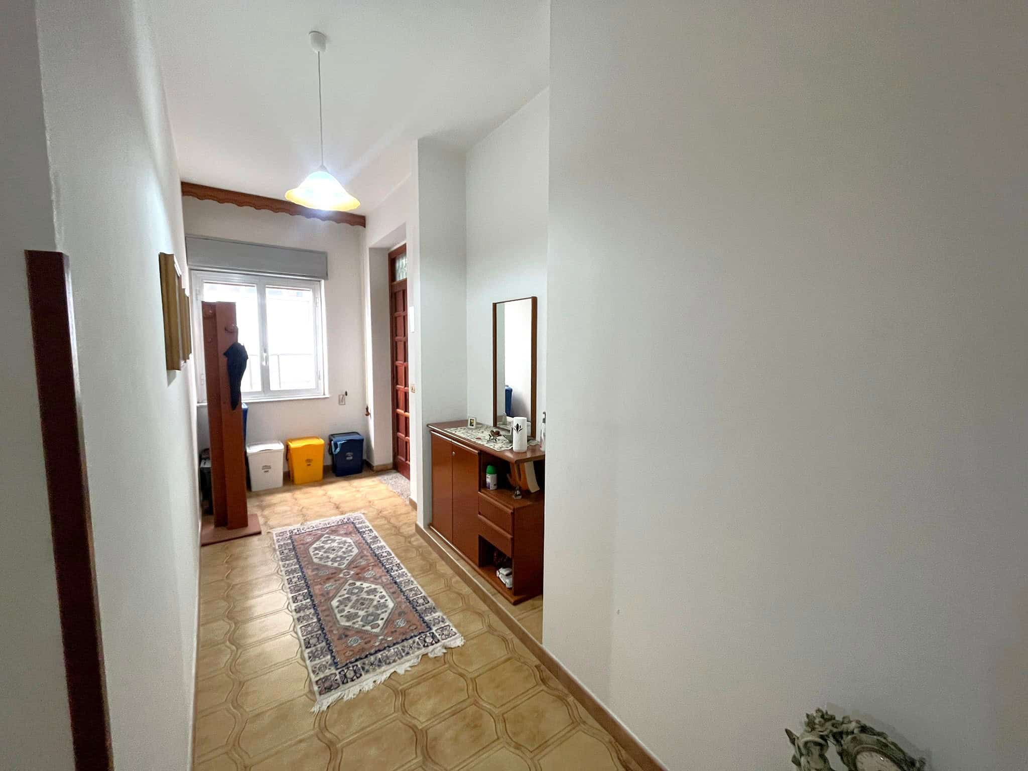 Interno di un appartamento con ingresso, corridoio e zona giorno luminosa, arredato con mobili moderni, tappeto decorativo e illuminazione a soffitto, vista verso la finestra con vista sulla città.