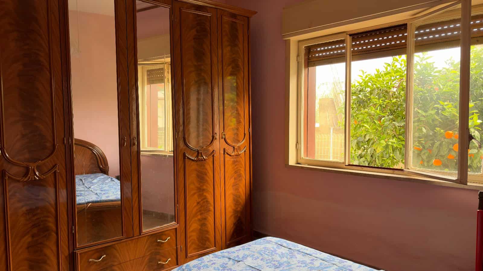 Armadio in legno massiccio con specchio e camera da letto con finestra che mostra un giardino verde.