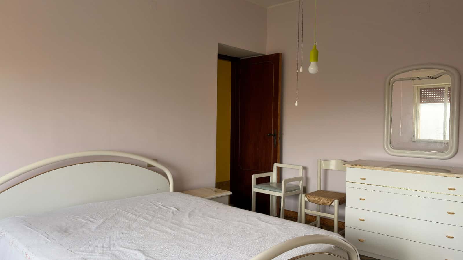 Letto matrimoniale con testiera bianca in una camera da letto luminosa e moderna, con pareti beige e arredi semplici.