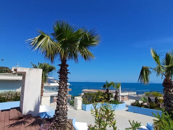 Spiaggia con palme e vista mare sotto un cielo azzurro, in un'area residenziale moderna.