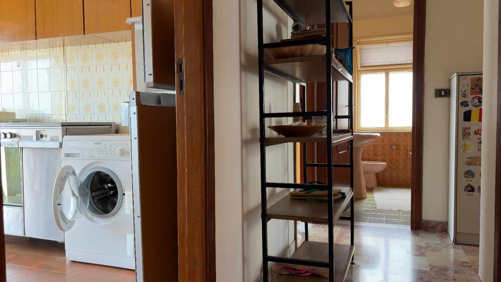 Lavanderia domestica con lavatrice e scaffali in metallo, ambiente luminoso e funzionale.