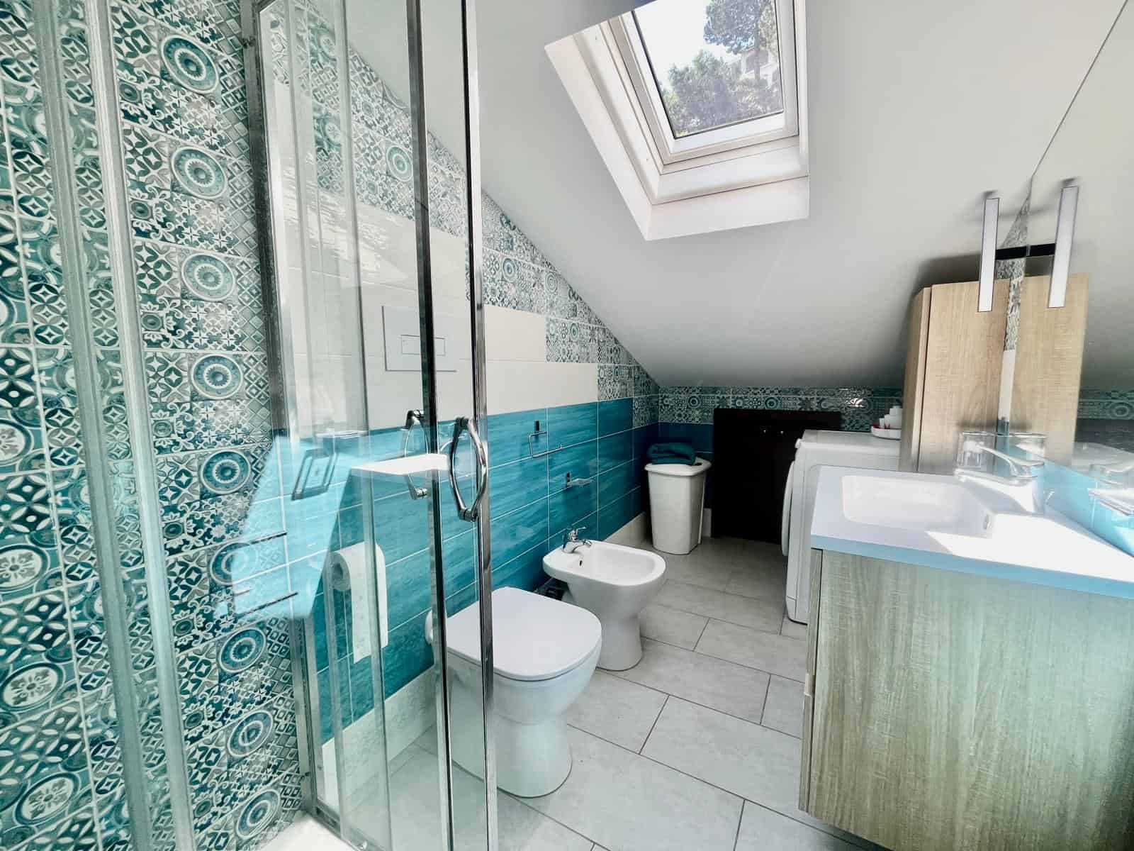 Bagno con finestra sul tetto, piastrelle decorative e arredi moderni, ideale per case di alta qualità. Design funzionale e luminoso, perfetto per ambienti di comfort e stile.