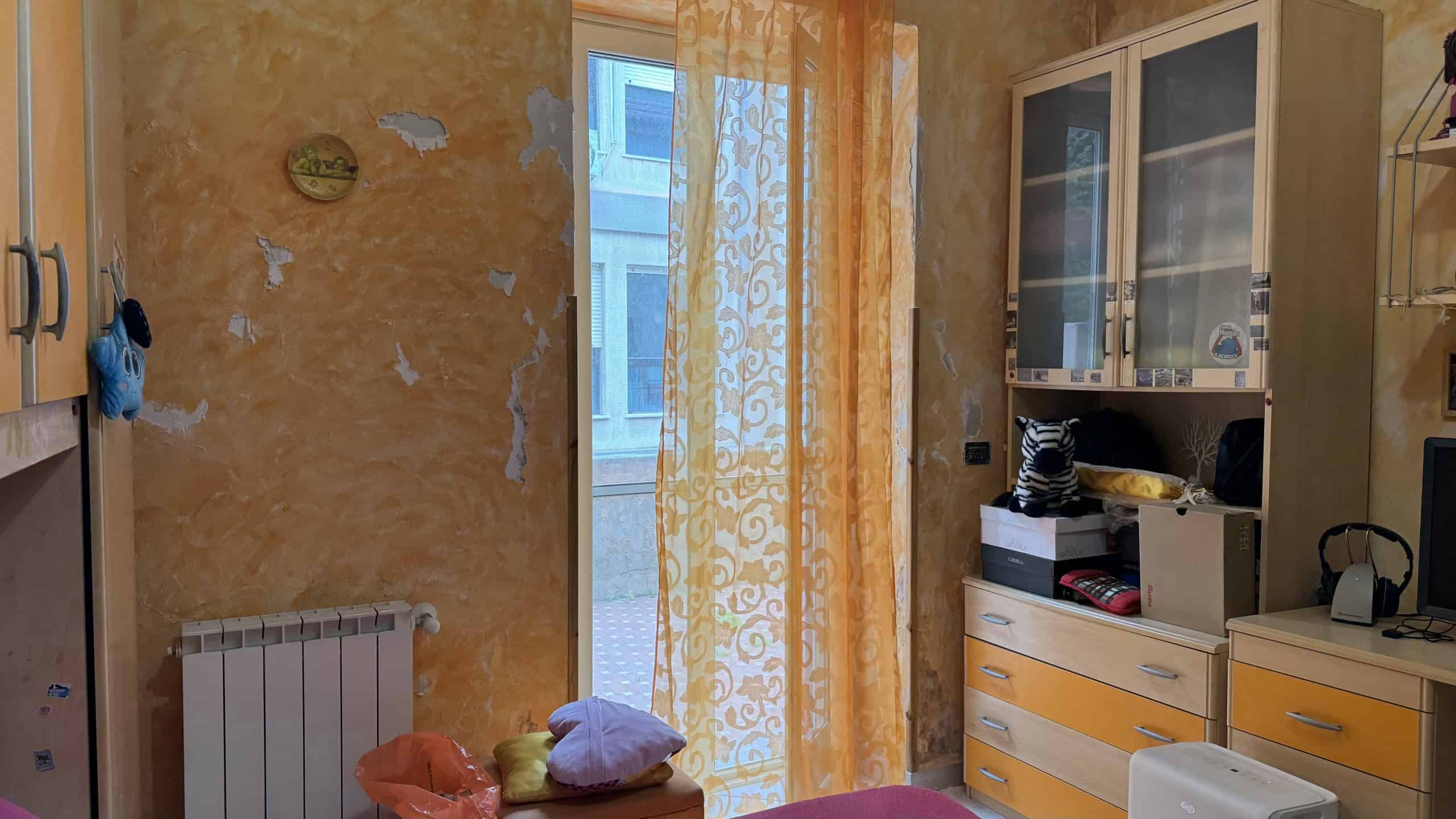 Ampia vista di un soggiorno luminoso con pareti color terracotta, finestra con tende gialle e arredi moderni in stile minimalista, ideale per la vendita o l'affitto di immobili residenziali.