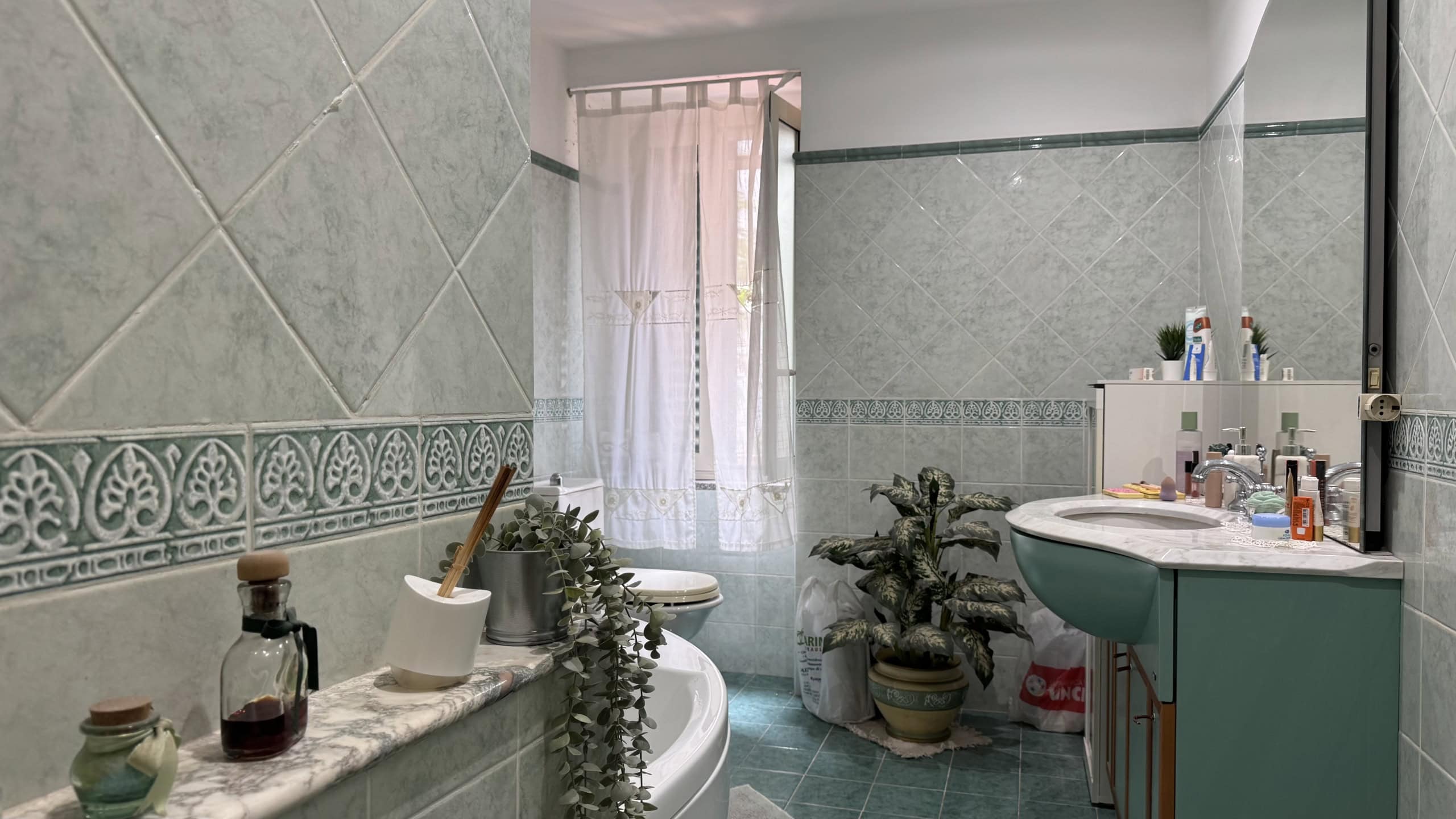 Lavabo e specchio in bagno con piastrelle verdi e decorazioni, ambiente luminoso e accogliente, ideale per la cura personale e il relax quotidiano.