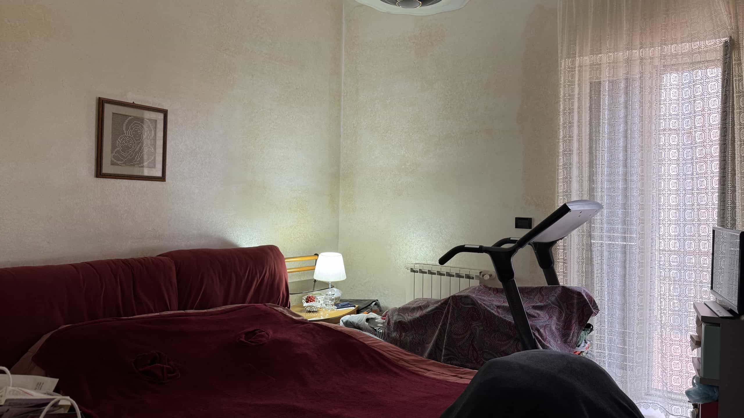 Spazio abitativo con letto matrimoniale, lampada da tavolo e finestra con tende leggere, ambiente accogliente e luminoso, ideale per soggiorni confortevoli e rilassanti.