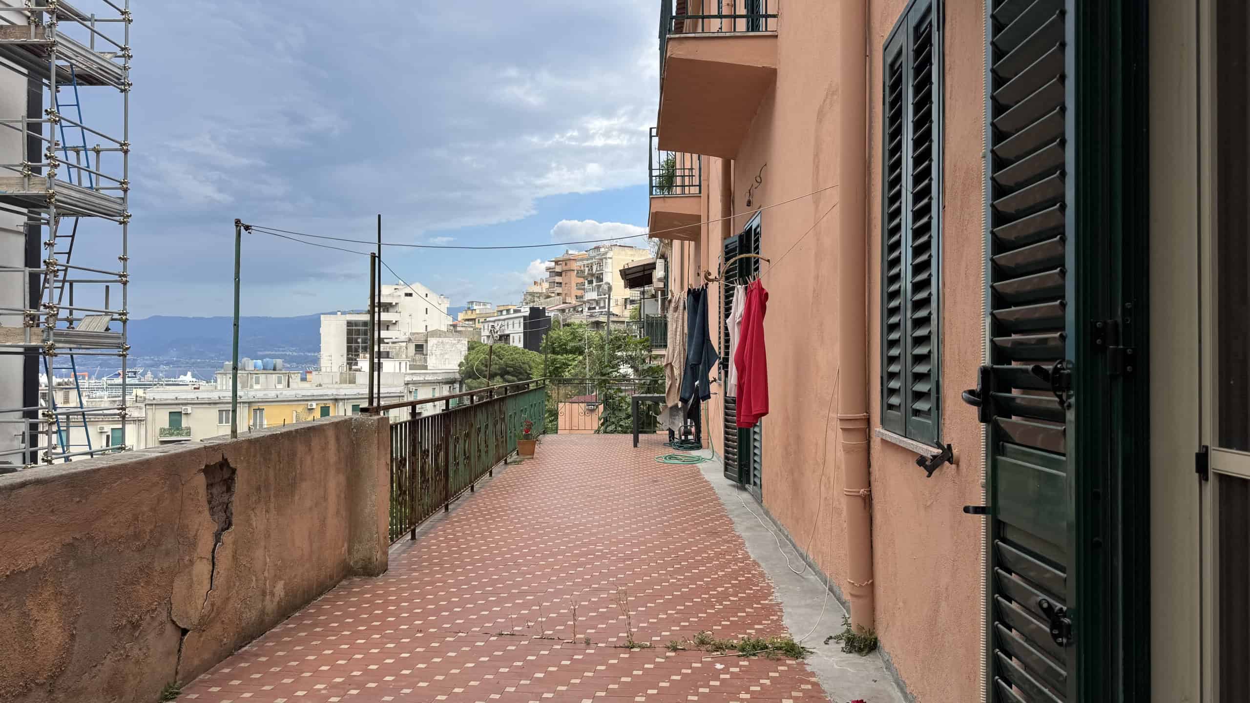 Ampio balcone con vista sulla città e sul mare, con pavimentazione in piastrelle rosse e ringhiera in ferro, in un edificio residenziale in Italia.