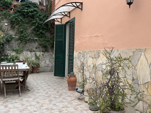 Elegante cortile esterno con arredi in legno, piante e decorazioni in terracotta, ideale per relax e convivialità, in un contesto residenziale italiano.