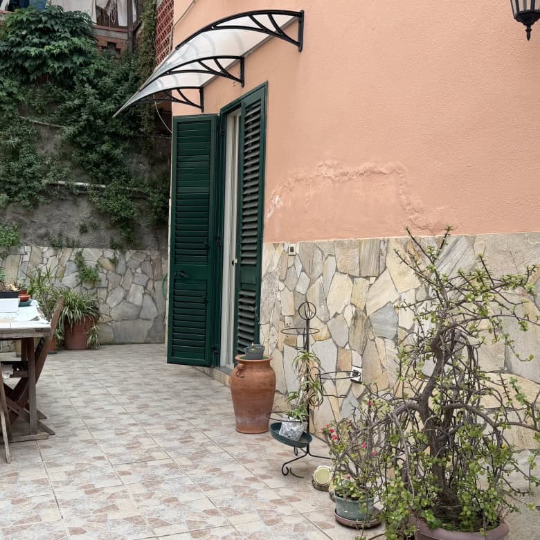 Elegante cortile esterno con arredi in legno, piante e decorazioni in terracotta, ideale per relax e convivialità, in un contesto residenziale italiano.