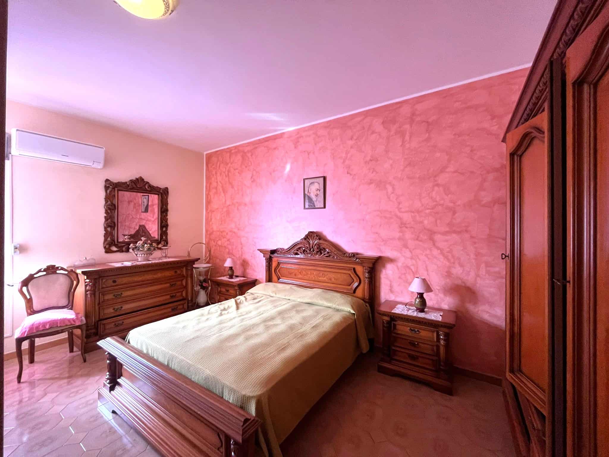 Camera da letto elegante con mobili in legno massiccio, pareti rosa e arredi classici, ideale per case di lusso e appartamenti di alta qualità.