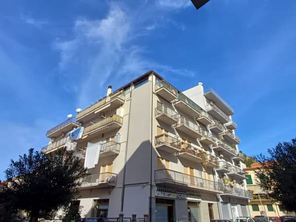 Appartamento residenziale con balconi e aria aperta, edificio moderno in zona urbana soleggiata, cielo blu e alberi circostanti, ideale per investimento immobiliare o abitazione privata.