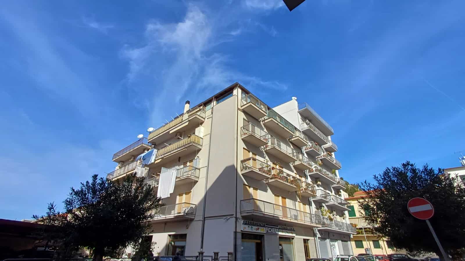 Appartamento residenziale con balconi e aria aperta, edificio moderno in zona urbana soleggiata, cielo blu e alberi circostanti, ideale per investimento immobiliare o abitazione privata.