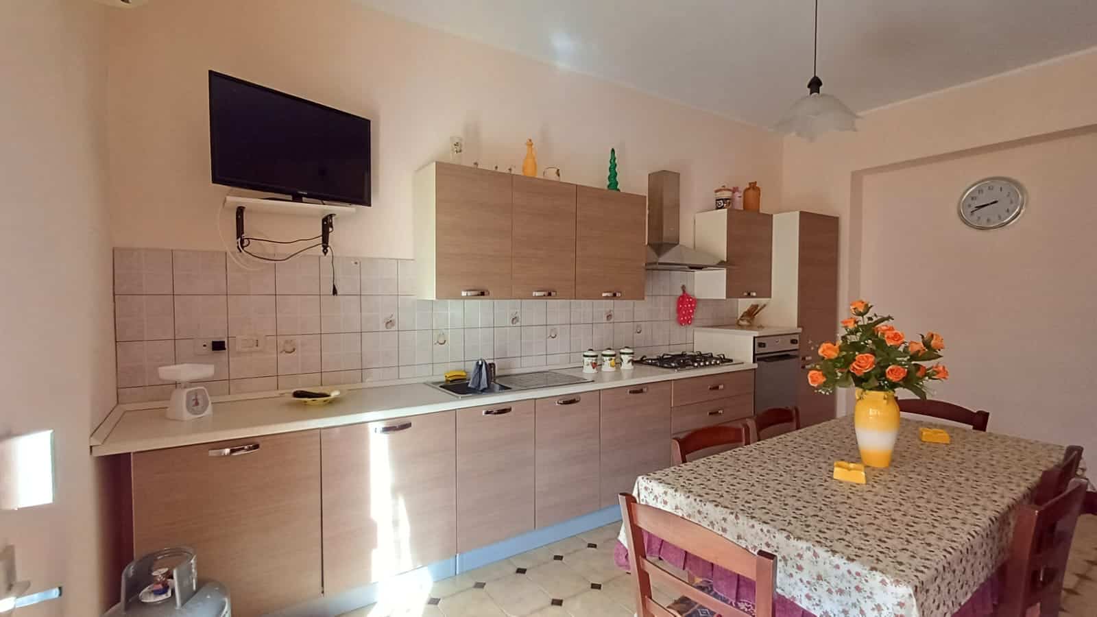 Cucina moderna con mobili in legno chiaro, piano di lavoro spazioso, pareti beige e accessori decorativi, ideale per famiglie e appassionati di cucina.