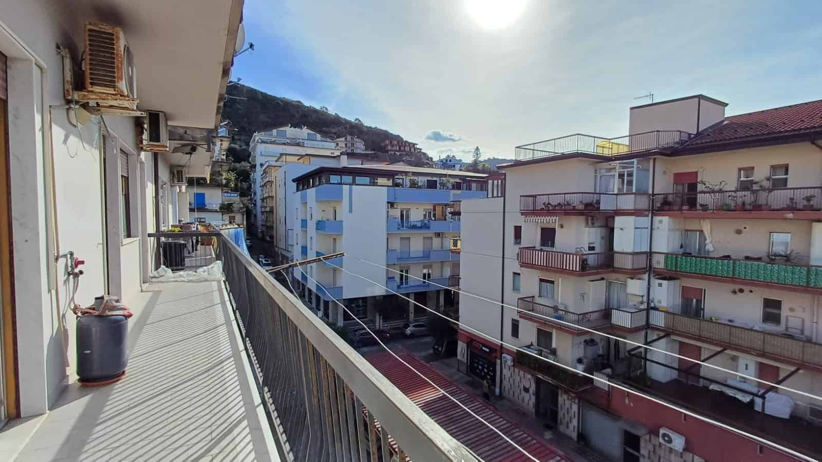 Balcone di un appartamento con vista su edifici residenziali e montagne sullo sfondo, in un contesto urbano di Napoli, Italia.