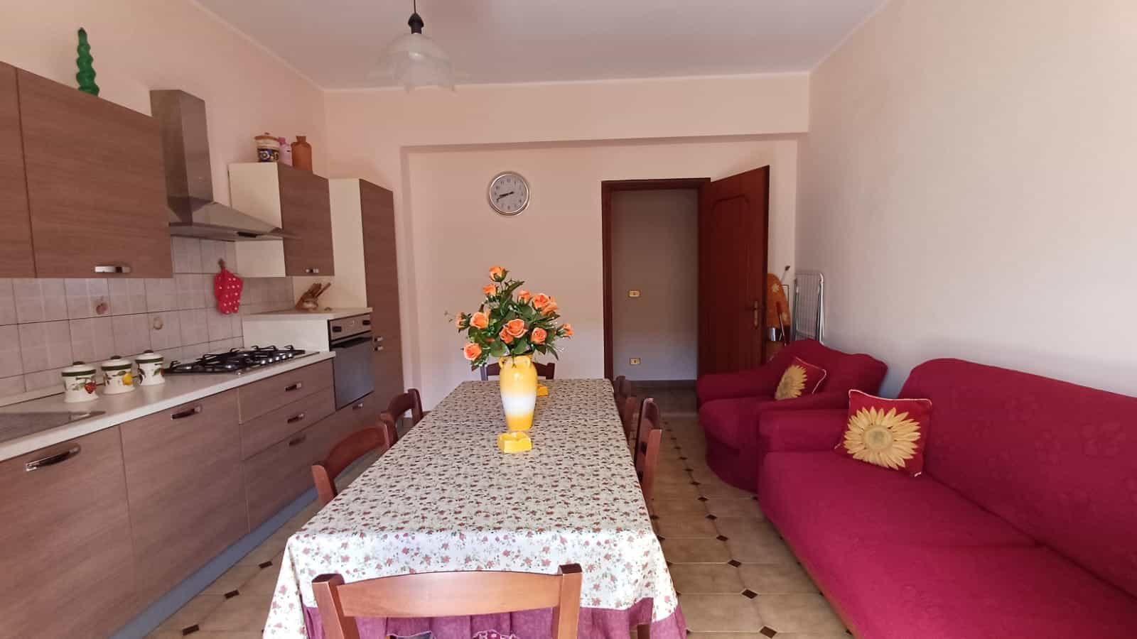 Aggiunta di un'ampia sala da pranzo e soggiorno con cucina moderna, mobili in legno, divano rosso e decorazioni floreali, ideale per vivere e ricevere ospiti in un ambiente accogliente e funzionale.
