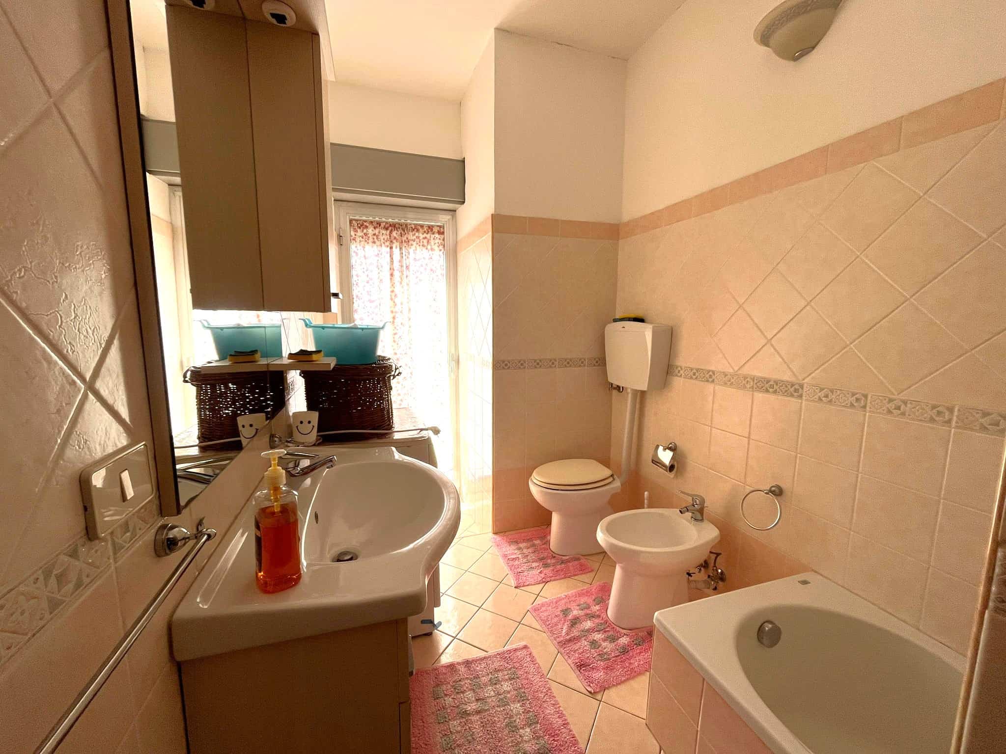 Lavabo e servizi igienici in bagno spazioso con piastrelle beige, bidet e vasca da bagno, ambiente luminoso e accogliente, ideale per appartamenti in affitto o vendita a NextCasa.