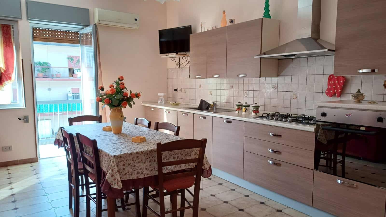 Cucina moderna con tavolo da pranzo, sedie in legno, e balcone con vista mare, ambiente luminoso e accogliente.
