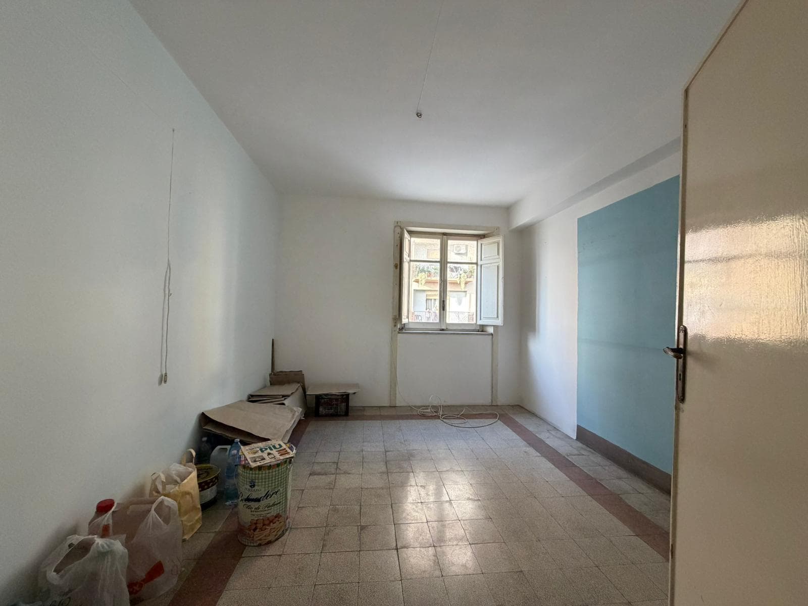 Stanza vuota in affitto o vendita con pareti bianche, finestra e pavimento in piastrelle, ambiente luminoso e spazioso, ideale per residenza o ufficio.