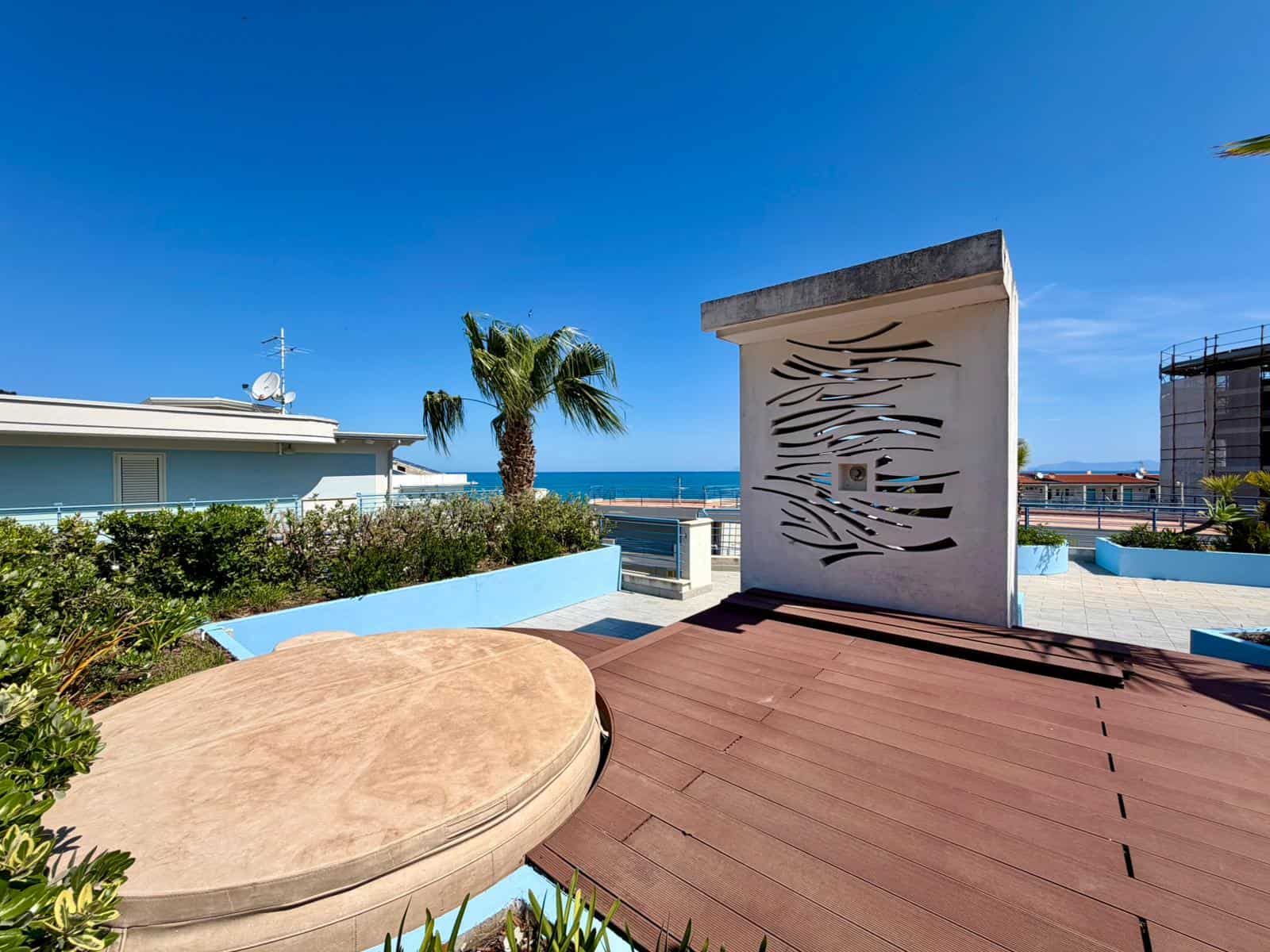 Esterno di un terrazzo con vista mare, elementi di design moderno e piante tropicali, ideale per relax e convivialità in un contesto residenziale di lusso.