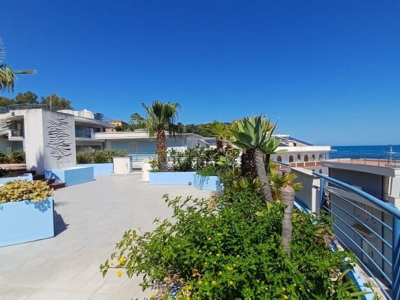 Spiaggia e vista mare dal complesso residenziale NextCasa con palme e architettura moderna, ideale per vacanze al mare in Italia.