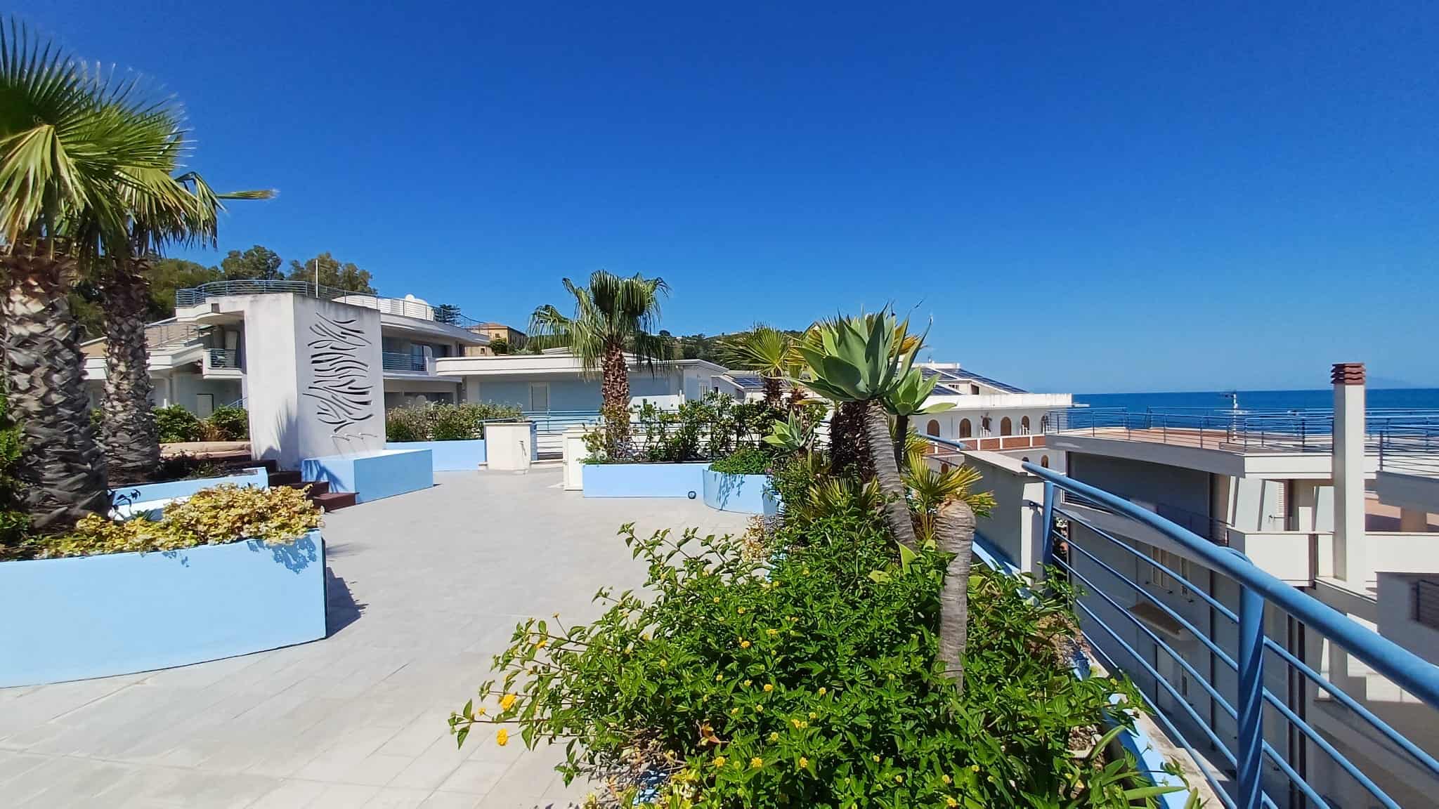 Spiaggia e vista mare dal complesso residenziale NextCasa con palme e architettura moderna, ideale per vacanze al mare in Italia.
