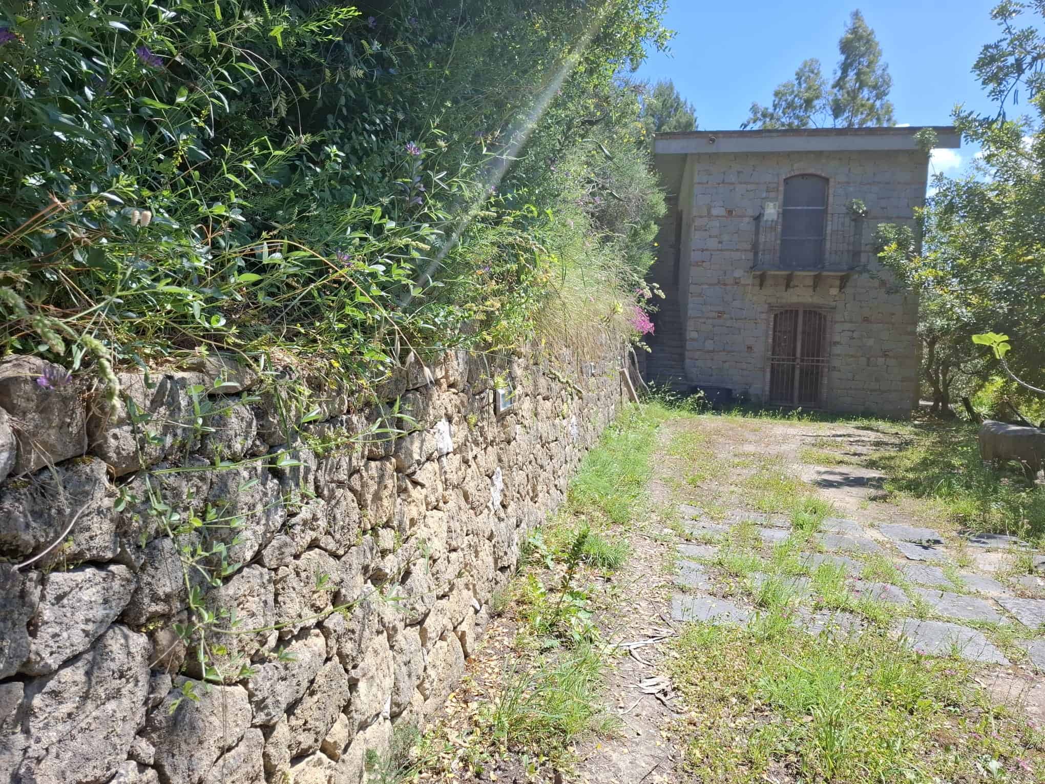 Casa storica in pietra con giardino e vialetto in pietra, immersa nel verde.