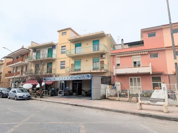 Edificio residenziale con negozio al piano terra, in una strada urbana, con auto parcheggiate e negozio di alimentari.